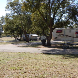Relax in a shady green RV spot surrounded by tall trees in a quiet wooded area.